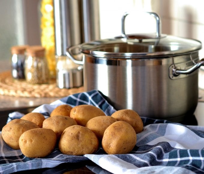 Potatoes beside a cooking pot with spices in the background.